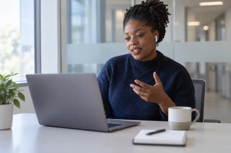 Fundraiser in earbuds talking through a practice conversation at a laptop, with a notebook and coffee on the desk